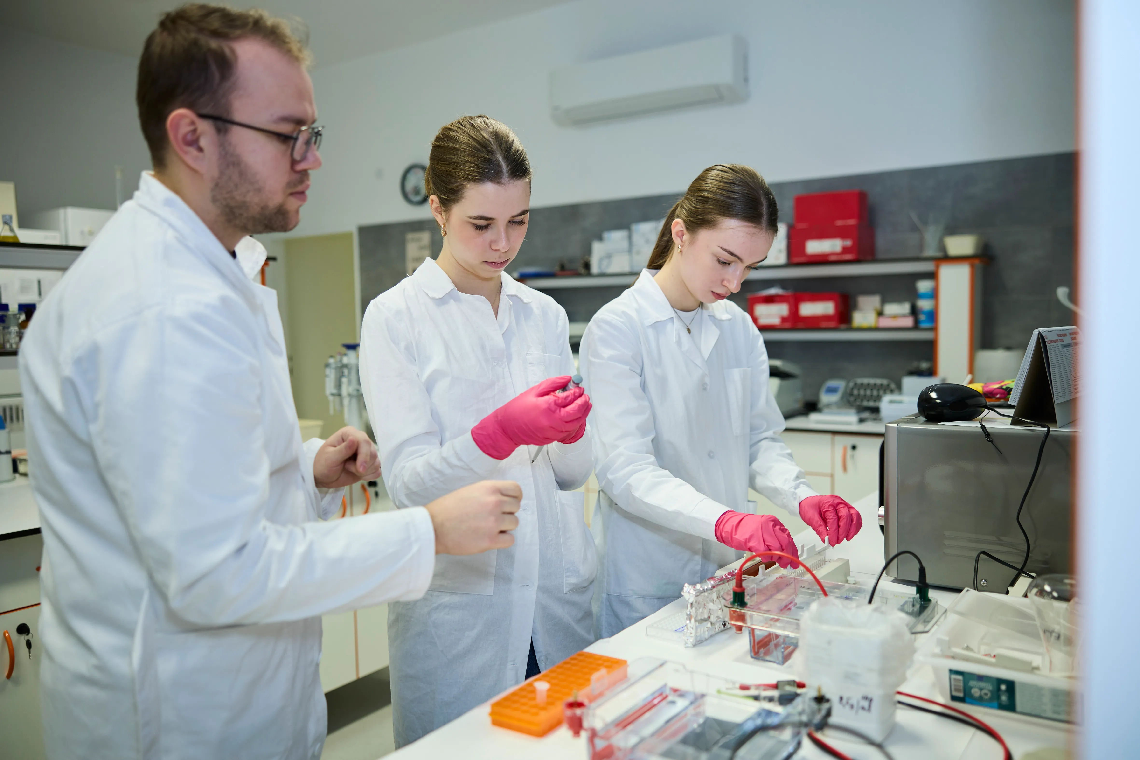 Vedecký mentor a študentky pri experimente v laboratóriu  can you write meta title and meta description for this blog Mladé vedkyne, ktoré menia pohľad na plasty: Ako stredoškoláčky bojujú za zelenšiu budúcnosť V našej spoločnosti pevne veríme, že udržateľnosť nie je len slovo, ale záväzok voči budúcim generáciám. Skutočná zmena však neprichádza sama od seba, formuje sa v rukách ľudí, ktorí majú odvahu hľadať inovatívne riešenia ekologických výziev. Sme nesmierne hrdí, že v rámci našej iniciatívy na podporu komunitných a zelených projektov sme sa stali partnermi výnimočného projektu "Výcvikové laboratórium mladých vedcov pre zelené biotechnológie". Tento projekt dal priestor mladej a inšpiratívnej dvojici stredoškoláčok, ktoré sa rozhodli venovať svoj voľný čas téme, ktorá trápi celú našu planétu: biodegradácii plastového odpadu pomocou baktérií. Spojili sme sa s nimi, aby sme vám priblížili ich cestu, výskum a obrovskú dávku odhodlania, ktorú do projektu vkladajú. Cesta k vede a hľadanie ekologických riešení Prečo sa dve mladé dievčatá, Natália Mišenková a Ema Polčová z Gymnázia Gymnázia sv. Mikuláša v Prešove, rozhodli namiesto bežných stredoškolských záujmov tráviť hodiny v laboratóriu? Odpoveď je jednoduchá – vášeň pre biológiu, chémiu a túžba prispieť k riešeniu globálnych environmentálnych problémov. Pod odborným vedením a záštitou pani učiteľky Miriam Feretovej sa skontaktovali s univerzitou a pustili sa do náročného výskumu. „Chceme to študovať, tak sme si to chceli nejako priblížiť. Táto téma nás zaujala, keďže je to veľmi veľký problém v dnešnej dobe,“ vysvetľuje Ema Polčová motiváciu, ktorá ich poháňa vpred. V čom spočíva jedinečnosť ich výskumu?  Hoci svetová veda už pozná baktérie schopné rozkladať plasty, väčšina doterajších procesov prebieha pri veľmi vysokých teplotách, čo je energeticky aj ekonomicky náročné. Mladé vedkyne sa preto zamerali na hľadanie ekonomicky výhodnejších podmienok ako aj podmienok na urýchlenie degradácie plastov. •    Testovanie rôznych faktorov: Dievčatá neskúmajú len vplyv teploty, ale aj ďalšie dôležité podmienky, ako je pH či prítomnosť soli. •    Sila soli: Vzorky na výskum odoberali aj z okolia Prešova, konkrétne z oblasti Solivaru, kde sa kedysi ťažila soľ. Ich experimenty priniesli zaujímavé výsledky. Zistili, že vyššia koncentrácia soli podporuje rast jedného druhu baktérií. Doterajšie kľúčové objavy a výsledky výskumu: •    Ideálne podmienky a baktérie: Baktérie rodu Pseudomonas dosahovali najlepšie výsledky pri teplote 30 °C a pH 7–8.  •    Úspešnosť rozkladu: Biodegradovateľný plast po dvoch mesiacoch stratil takmer 89 % hmotnosti a po troch sa rozložil úplne. Pri bežnom polyetyléne zaznamenali úbytok o 12,5 %, zatiaľ čo ostatné testované materiály vykazovali len minimálne zmeny. •    Vizuálny dôkaz: Snímky zo skenovacieho elektrónového mikroskopu (SEM) jasne odhalili praskliny a povrchovú eróziu na plastoch po pôsobení baktérií. Získané výsledky naznačujú, že vybrané baktérie môžu predstavovať perspektívny nástroj pre ekologickejšie spracovanie plastového odpadu v budúcnosti.  Od laboratórneho stola na európske pódiá Ich úsilie a hodiny strávené výskumom už stihli žať prvé veľké úspechy. So svojím projektom úspešne zabodovali na domácom Festivale vedy a techniky. Tento úspech im otvoril dvere na EUCYS (European Union Contest for Young Scientists) jednu z najprestížnejších európskych súťaží pre mladých vedcov, ktorá sa v septembri uskutoční v nemeckom Kieli. Do tej doby dievčatá plánujú svoj projekt v laboratóriu neustále vylepšovať. Ich cieľ je jasný: „Čo najlepšie reprezentovať Slovensko, našu školu aj fakultu.“ Odhodlanie, balans a veľké sny o praxi Zladiť štúdium na strednej škole, testovanie v laboratóriu a bežný život tínedžera nie je jednoduché. Dievčatá úprimne priznávajú, že keď prebieha intenzívna fáza výskumu, musíte obetovať veľa voľného času a doháňať školské učivo po večeroch doma. Napriek tomu nestrácajú úsmev a hovoria o dôležitosti balansu medzi školou, vedou a oddychom. Keď sme sa ich opýtali na budúcnosť a reálne využitie v praxi, odpoveď Natálie Mišenkovej bola plná optimizmu: „Ak sa nám podarí nájsť ten správny bakteriálny kmeň, celý proces môžeme presunúť do veľkých nádrží - bioreaktorov. V uzavretých podmienkach baktérie bezpečne rozložia plasty bez toho, aby sme riskovali únik do prírody. Pred nami je ešte veľa práce a testovania. Ale ak chceme vo vede niečo skutočne zmeniť, musíme mať odvahu myslieť vo veľkom.“ Sme hrdí, že pomáhame rásť zeleným nápadom Stretnutia s takýmito mladými ľuďmi nás utvrdzujú v tom, že podpora lokálnych, ekologických a komunitných projektov má obrovský zmysel. Sme hrdí, že ako spoločnosť môžeme stáť pri zrode projektov, ktoré nielen chránia našu prírodu, ale zároveň formujú novú generáciu slovenských vedcov a lídrov v oblasti udržateľnosti. Dievčatám držíme palce na európskej súťaži v Kieli a budeme ich ekologickú cestu za čistejšou planétou aj naďalej pozorne sledovať a podporovať.