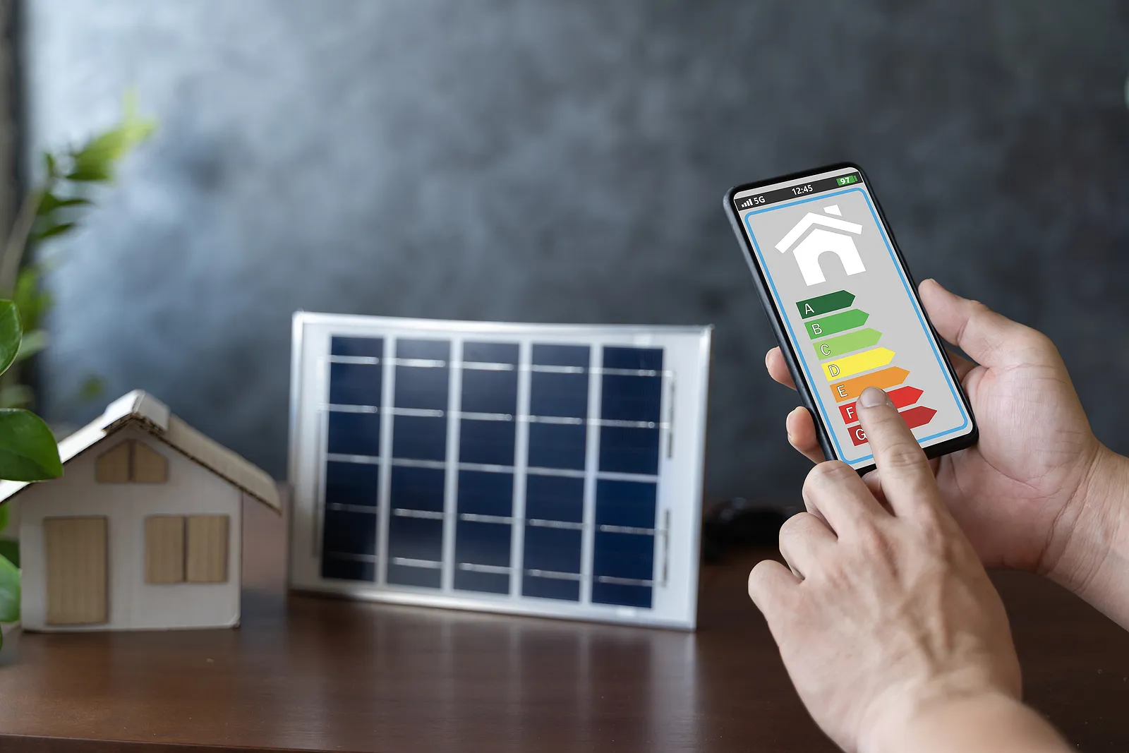 Človek držiaci mobil, na ktorom je zaznačená energetická naročnosť domu, za ním model fotovoltiky.