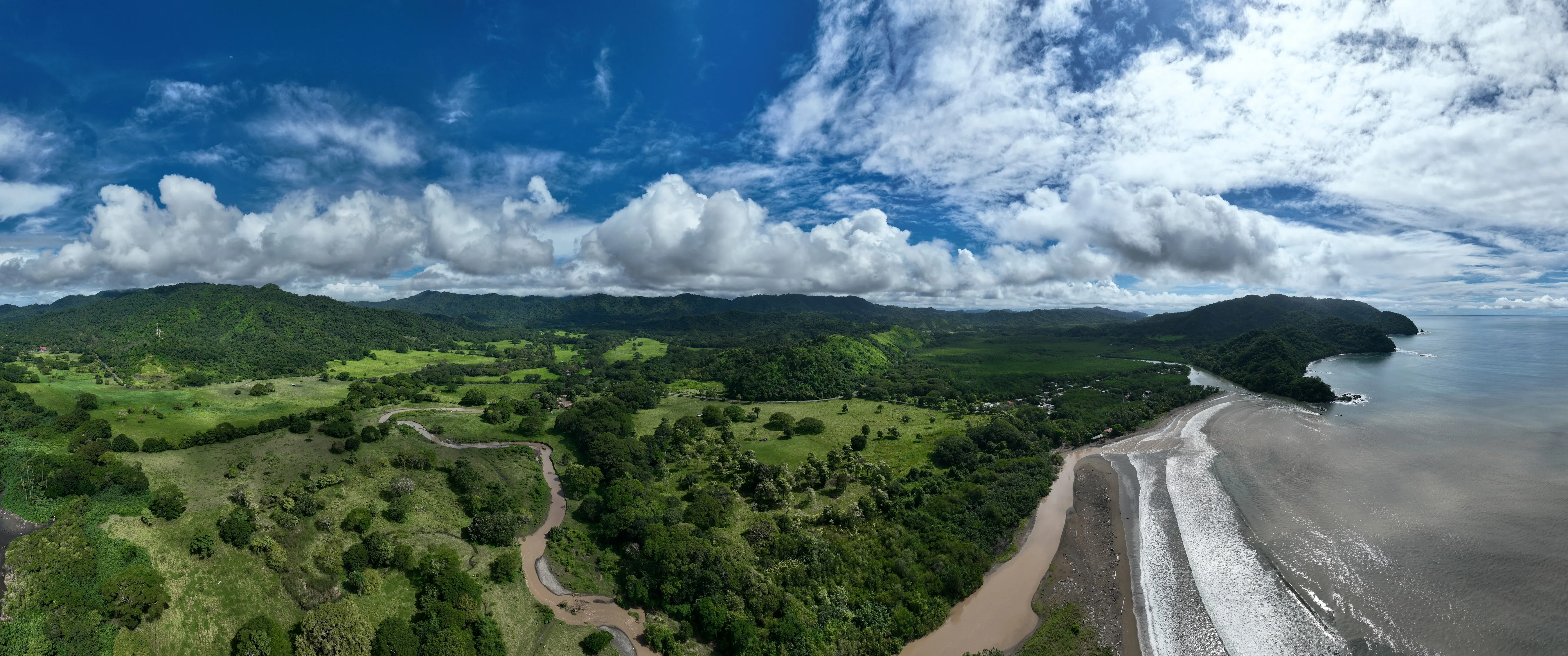 Pohľad zhora na zelenú krajinu a pobrežie oceánu s kopcami a prírodou typickou pre oblasti modrých zón.