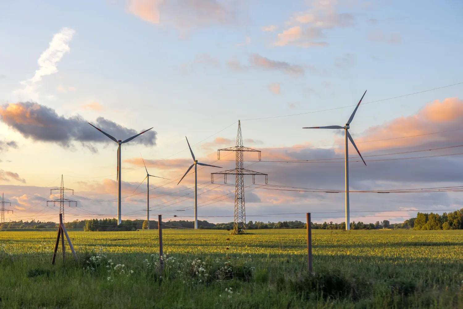 Veterné turbíny a stĺpy vysokého napätia na poli ako udržateľné obnoviteľné zdroje energie.